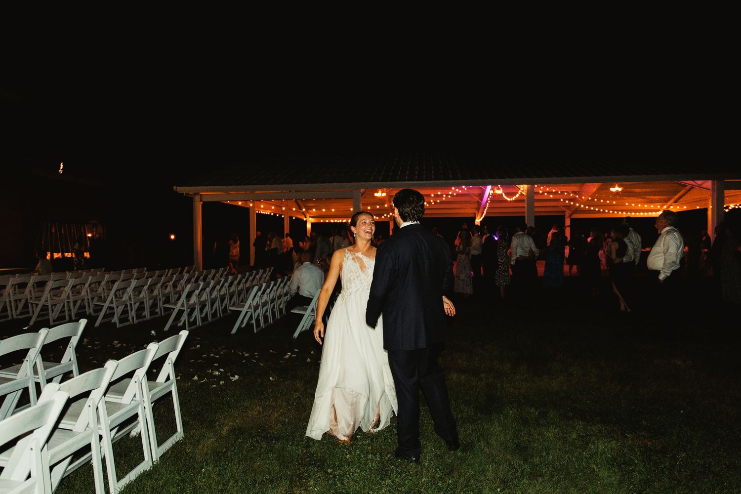 Outdoor wedding venue setup with white chairs and evening lighting.