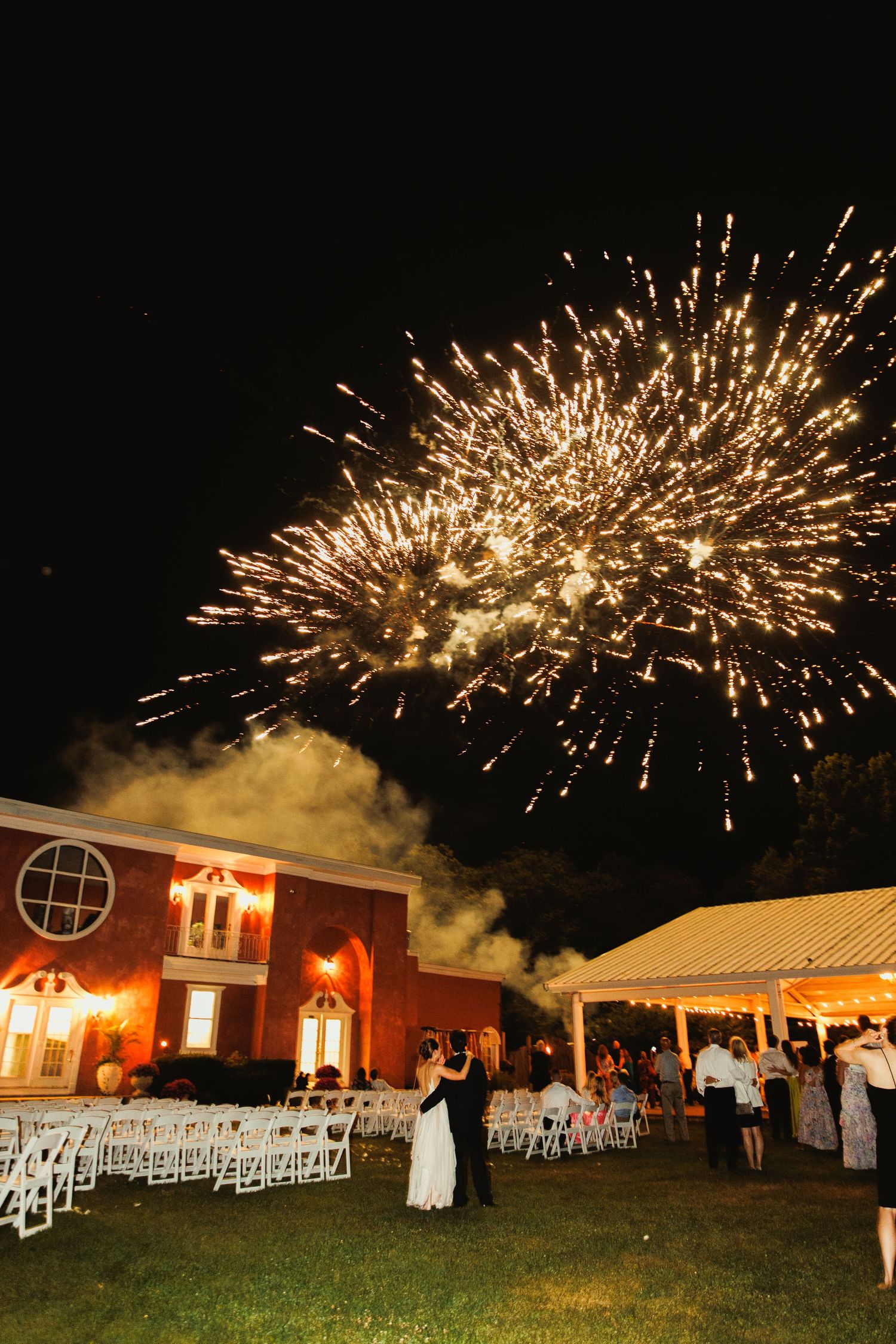 Golden fireworks illuminate the night sky above an elegant wedding reception venue.