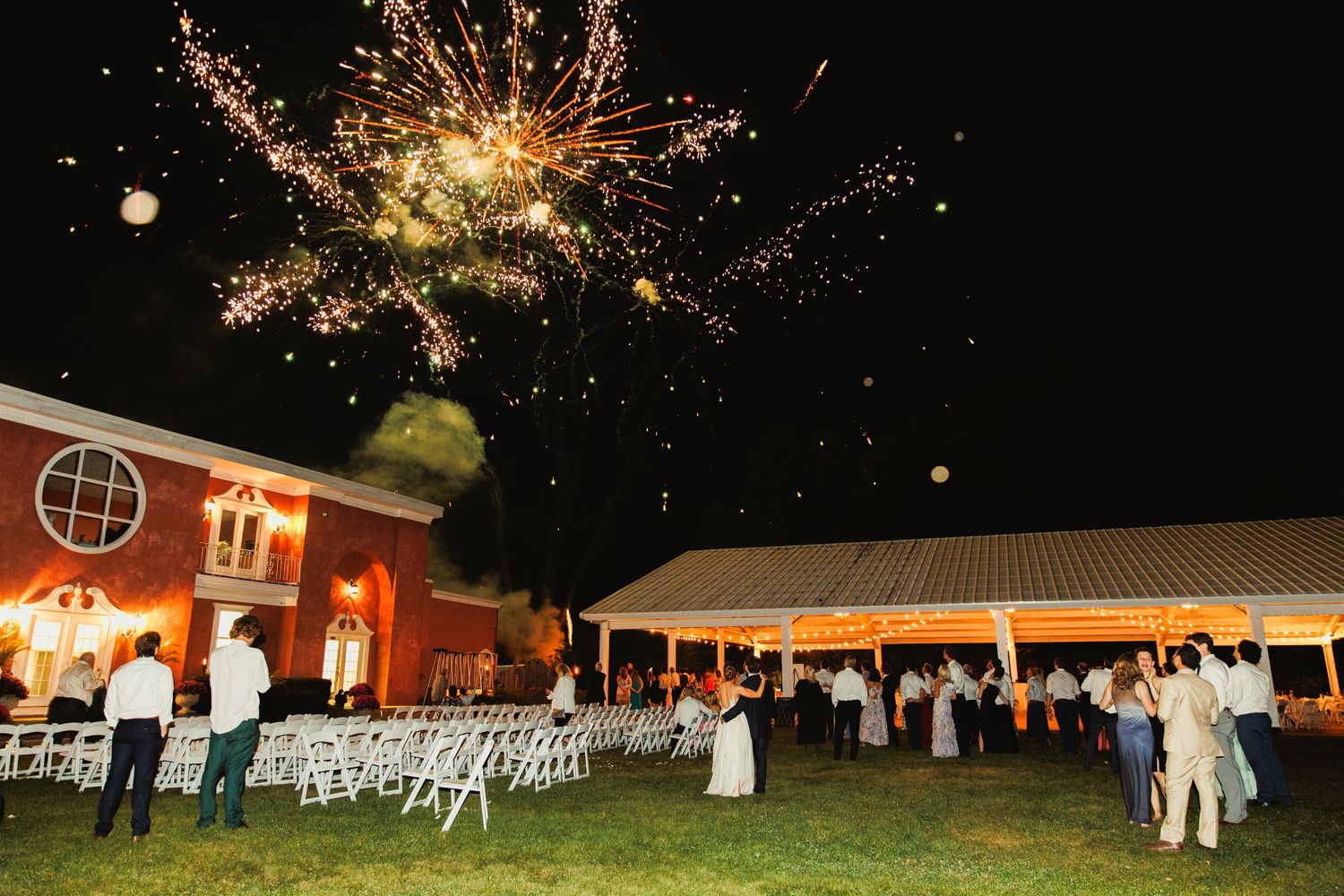 Colorful fireworks bursting in the dark sky above a wedding reception area.