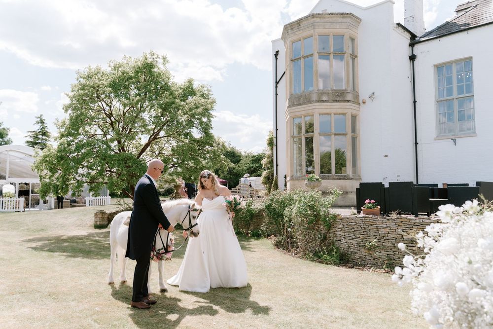 A couple shares a romantic moment outside a grand white building with a curved bay window on their wedding day.