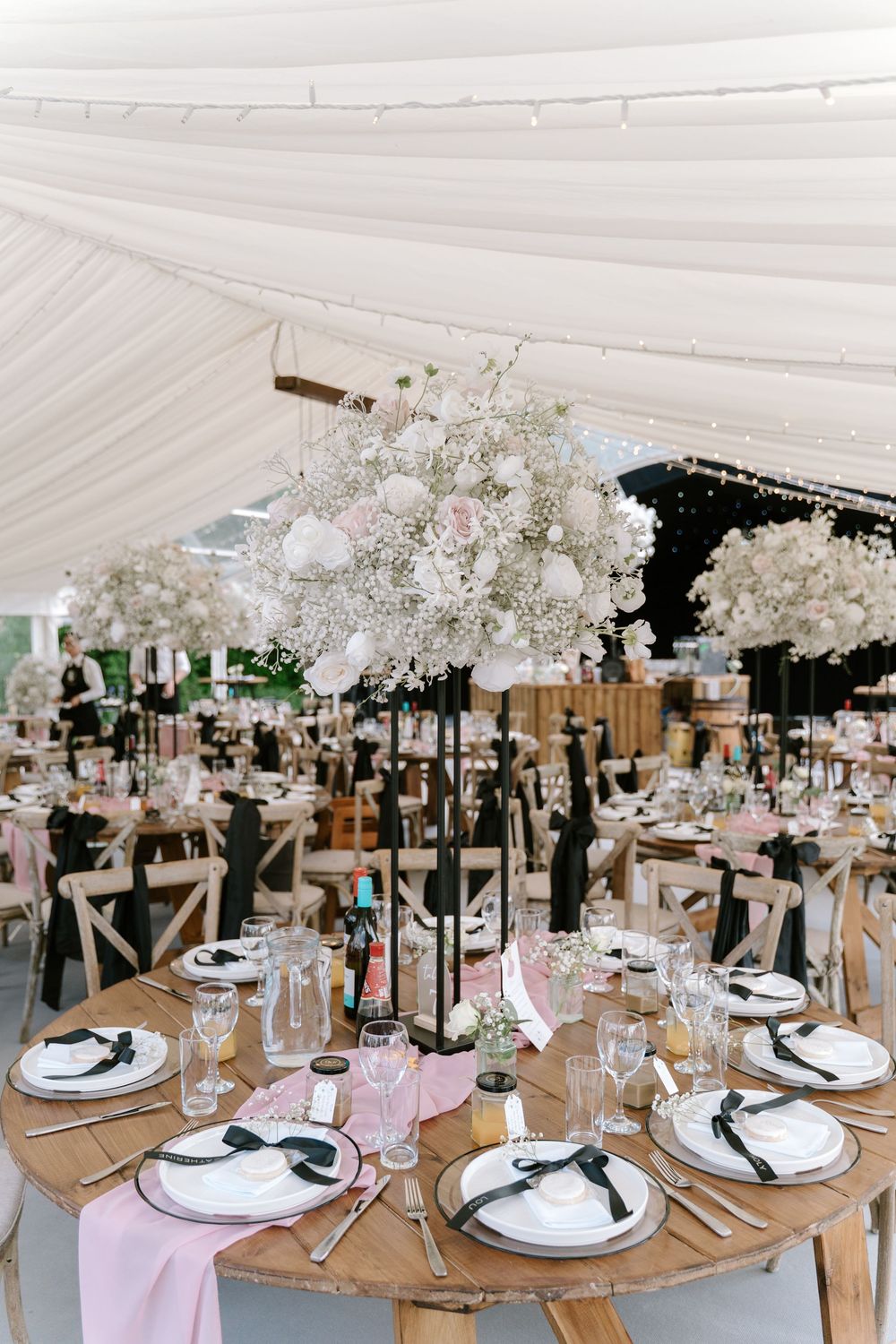 Elegant wedding reception tables set with white linens and floral centerpieces under a white tent canopy at Tywning park, Cotswolds.