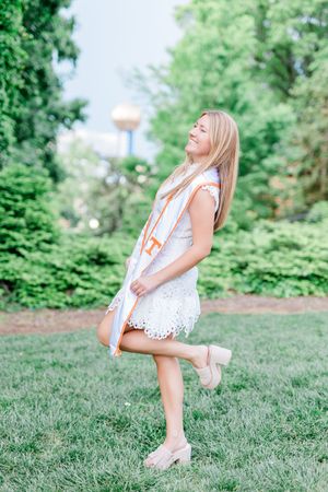 A person in a white lace dress twirls playfully on green grass in a summery outdoor setting.