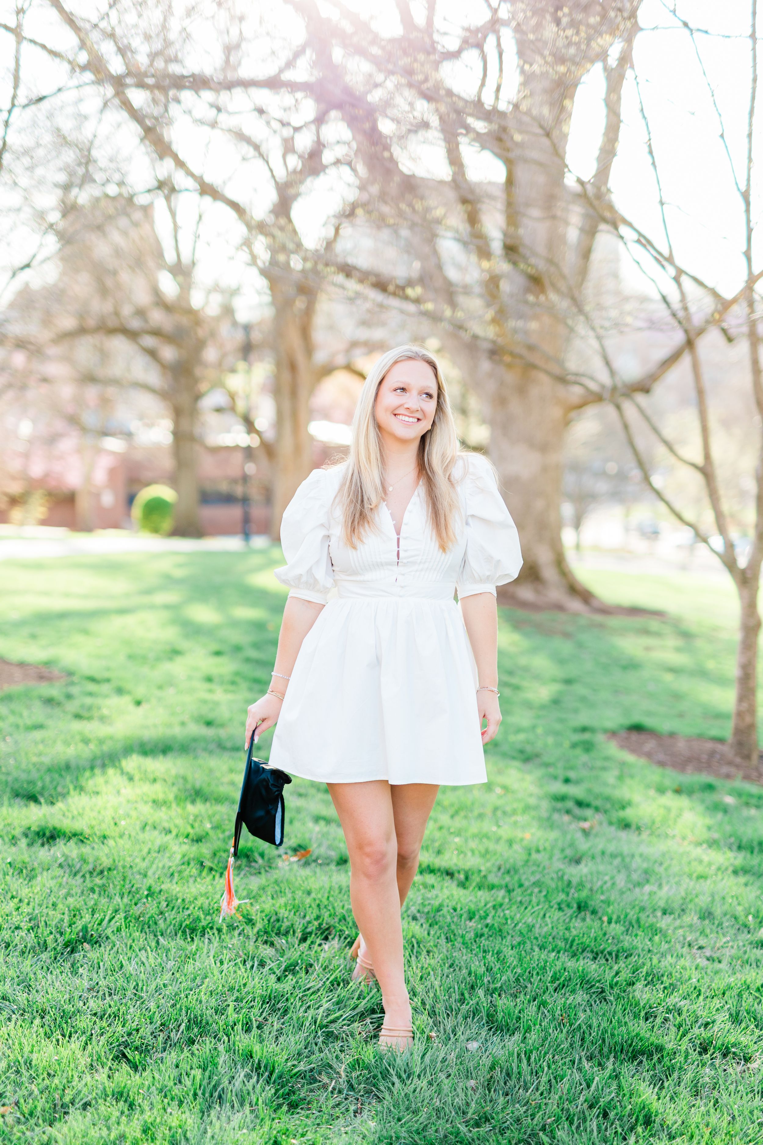 A person in a white dress walks barefoot through a grassy hillside on a spring day.