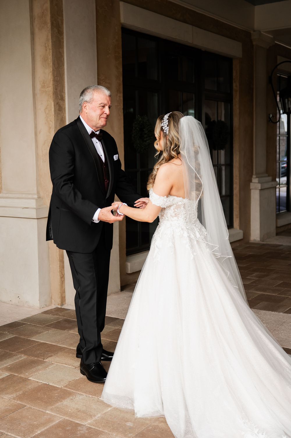 Touching first look sequence between bride and father in formal attire under covered portico.