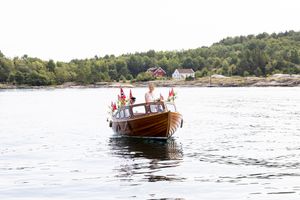 Bruden ankommer i båt til vielsen. Hun står fremme i en gammel snekke.