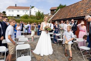 Bruden går mellom alle gjestene som har reist seg. Bruden har blomsterbukett og ser mot mannen sin.