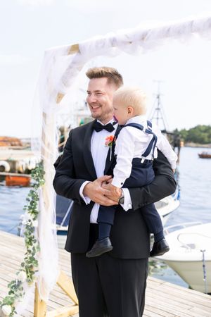 Brudgommen står med et barn på armen. Han ser mot bruden som kommer i mot han.
