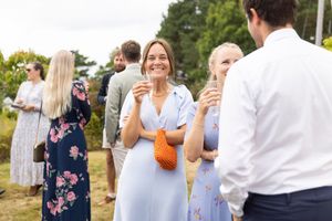 Bryllupsgjest i blå sommerlig kjole som smiler og holder et glass med bobler.
