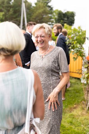 Øyeblikksbilde av brudens mor. Smiler og ler mot en annen bryllupsgjest.