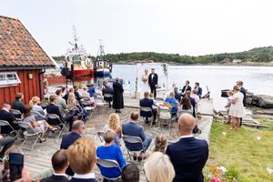 Oversiktsbilde av vielse som skjer på bryggekanten. De fleste gjestene sitter på klappstoler, men det står også noen mennesker langs kanten.