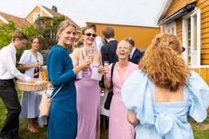 Sommerpyntede gjester som holder glass med bobler, ser rett i kamera og ler.