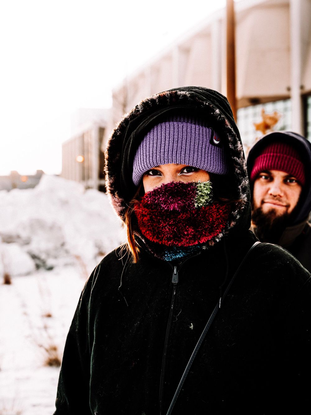 Group bundled in winter coats and hats standing in snowy conditions.