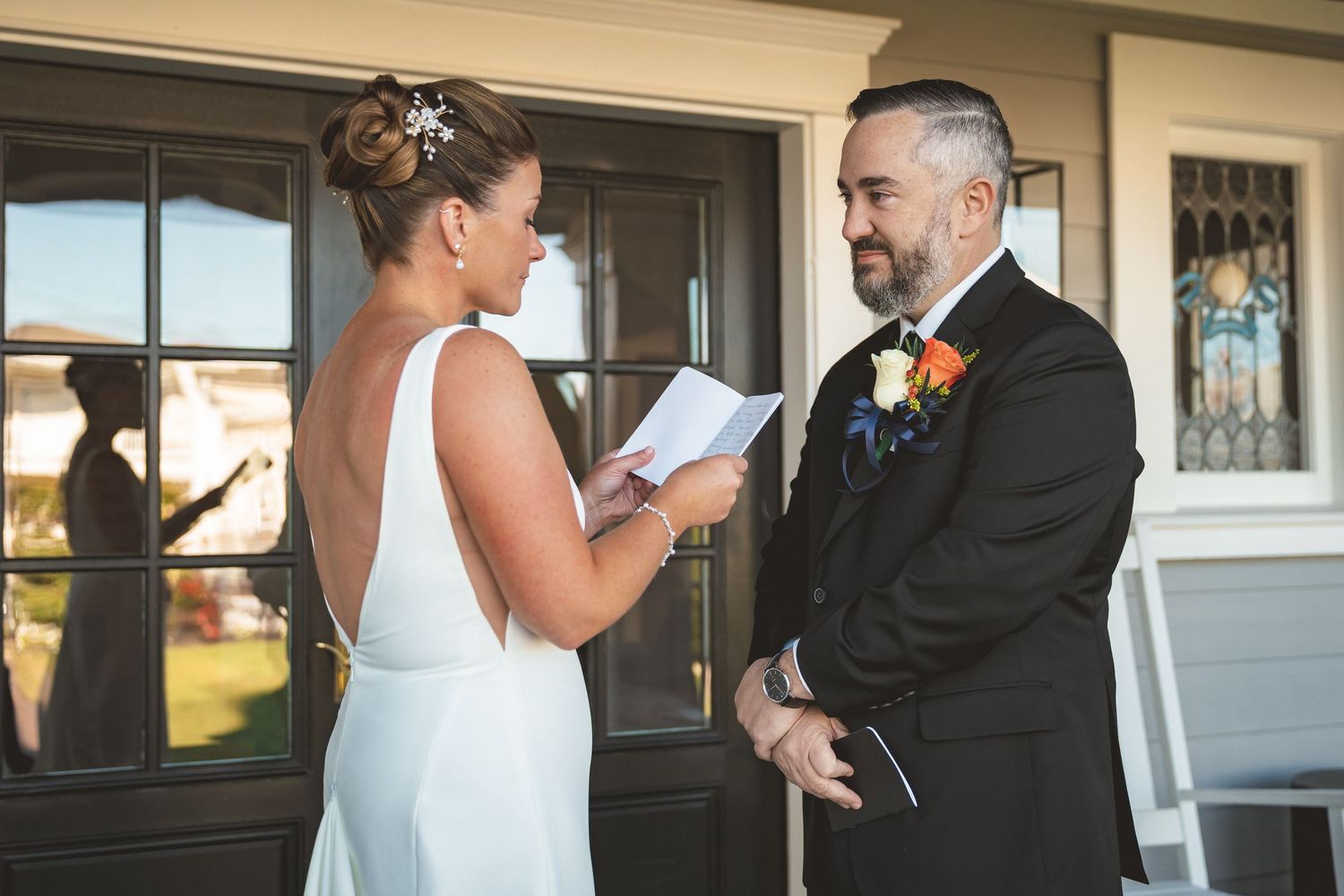 Bride reads wedding vows to groom in black suit during intimate outdoor ceremony.