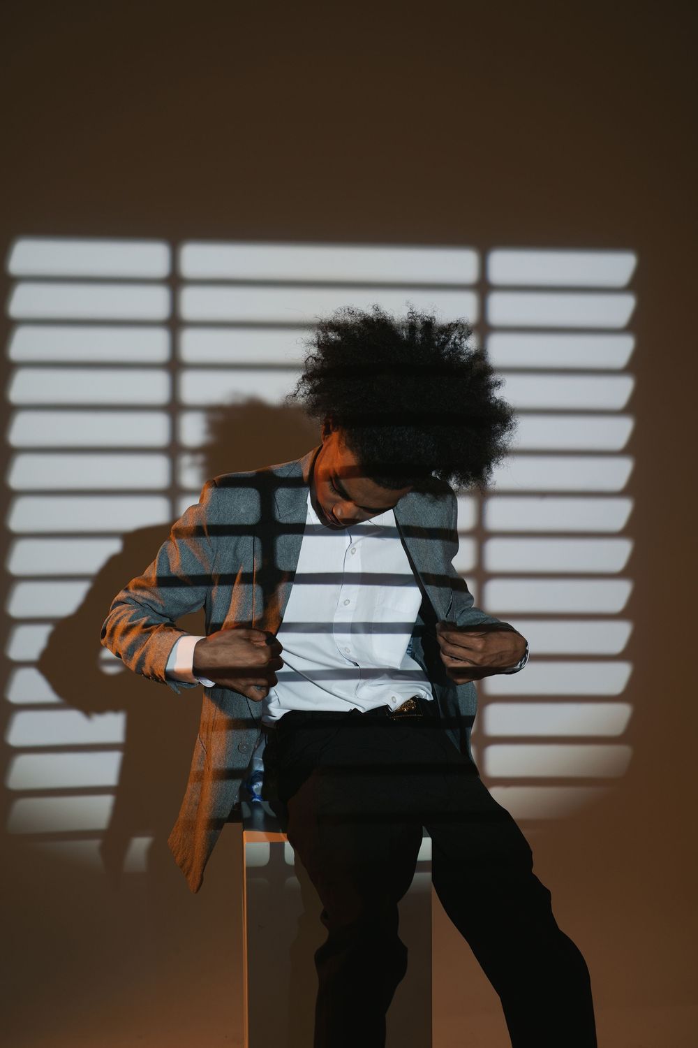 A sequence of silhouetted figures bending and moving against a wall with window blind shadows creating a dramatic pattern.