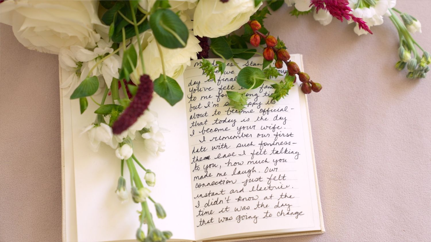 Handwritten note card surrounded by white and purple flowers with green foliage against a light background.