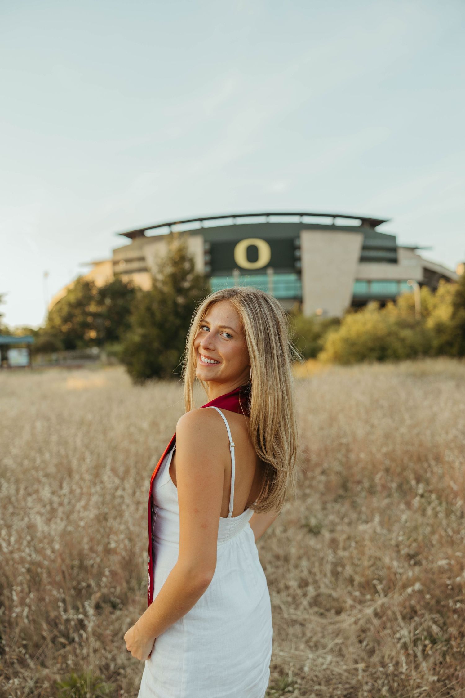 A person in a white tank top poses in a golden wheat field during sunset.