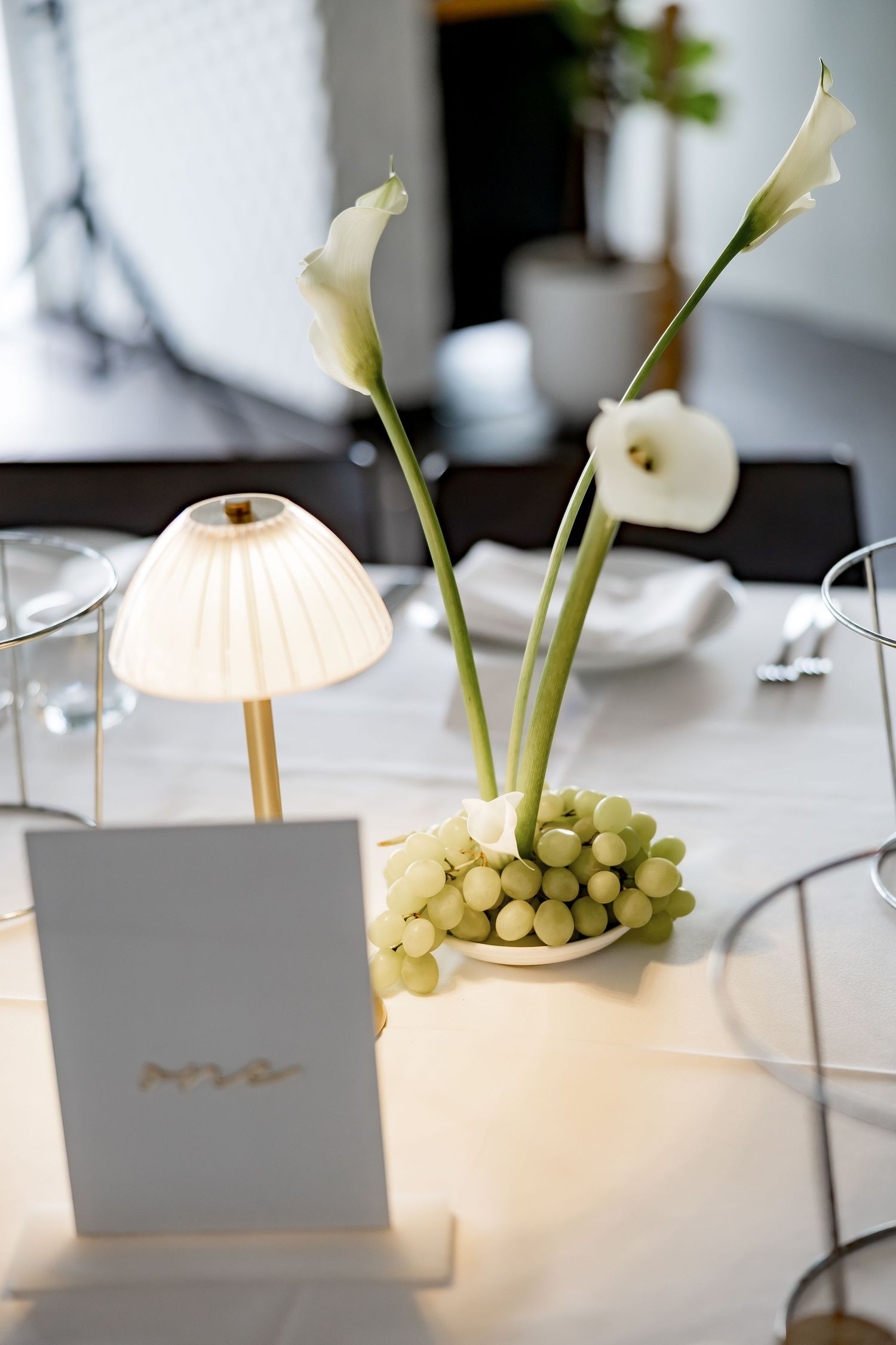 White calla lily flowers and green berries arranged on elegant table settings with soft lighting and place cards.