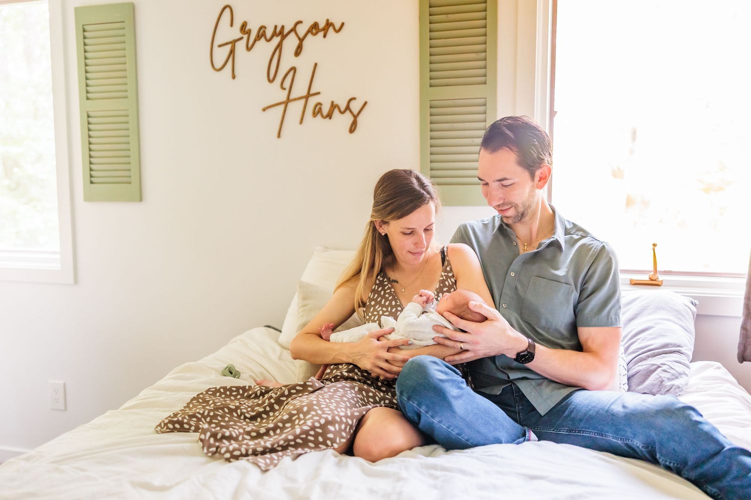 A couple sits together on a white bed with a leopard print blanket while looking at their phones.