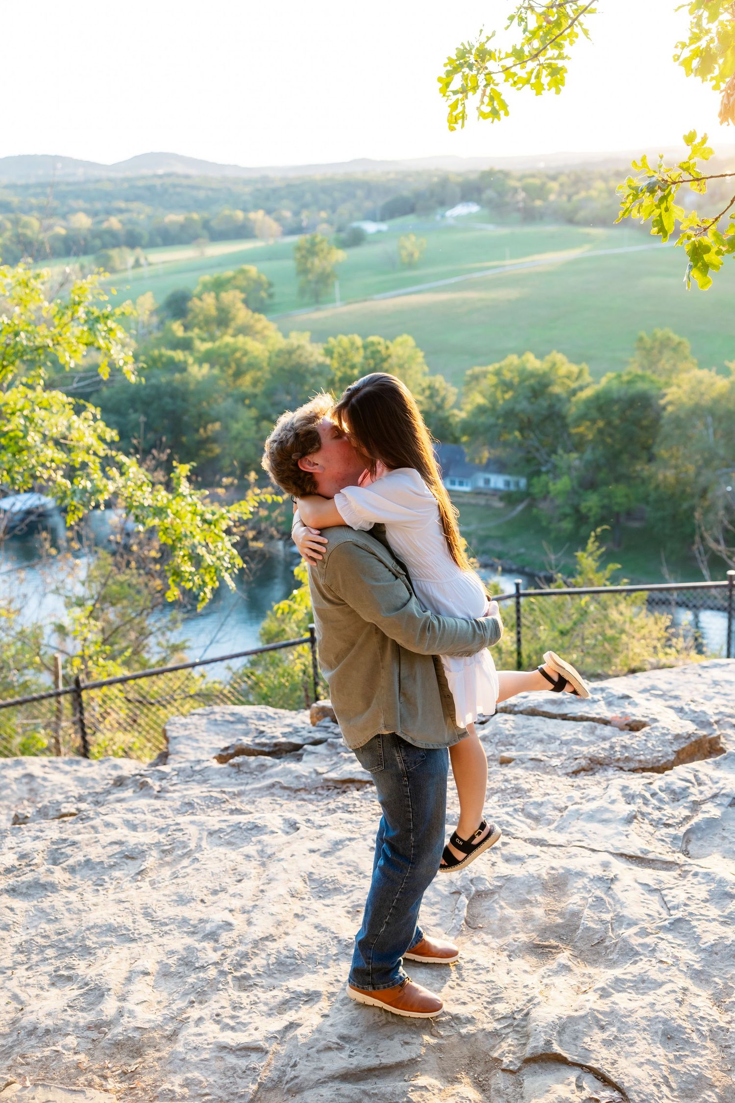 A couple stands together by a serene lake surrounded by autumn trees and mountains in the background.