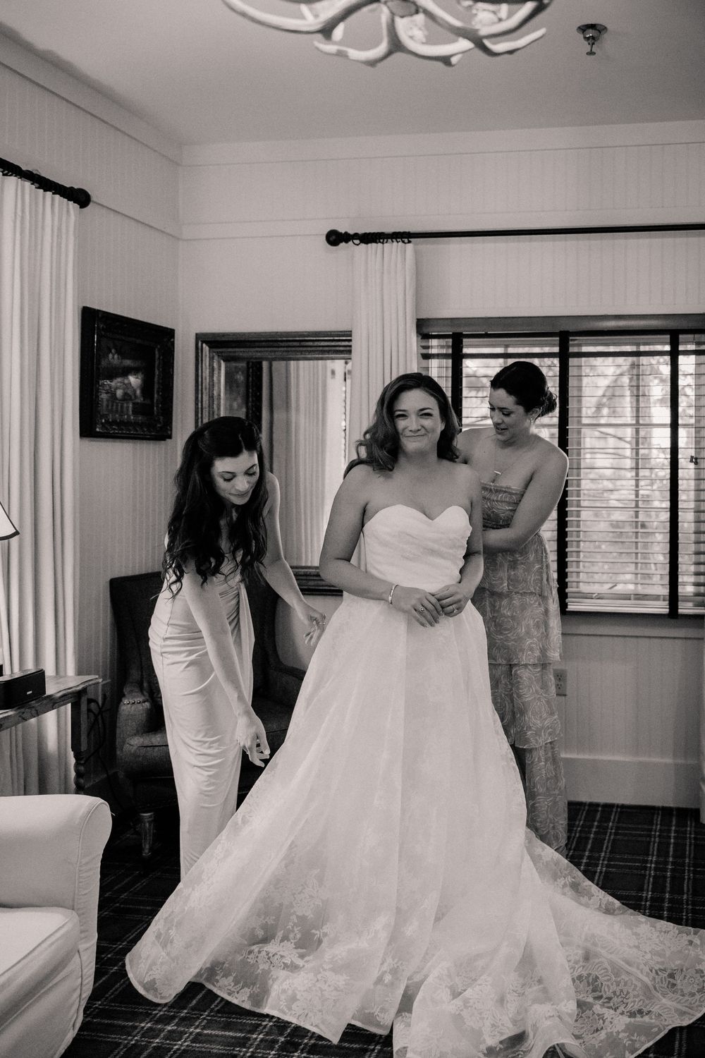 A bride gets help with her flowing white wedding gown in an elegant indoor setting.