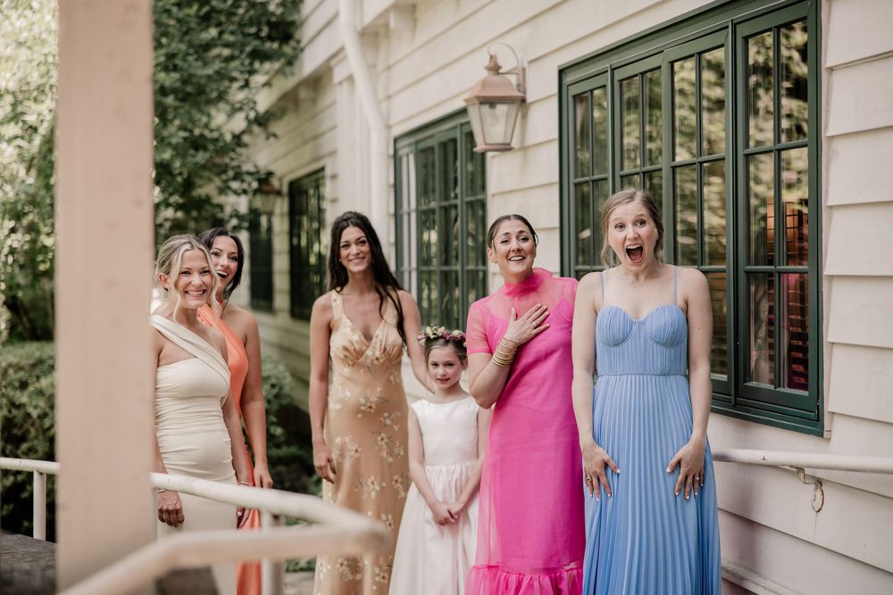 Bridesmaids in colorful dresses stand together outside a white building.