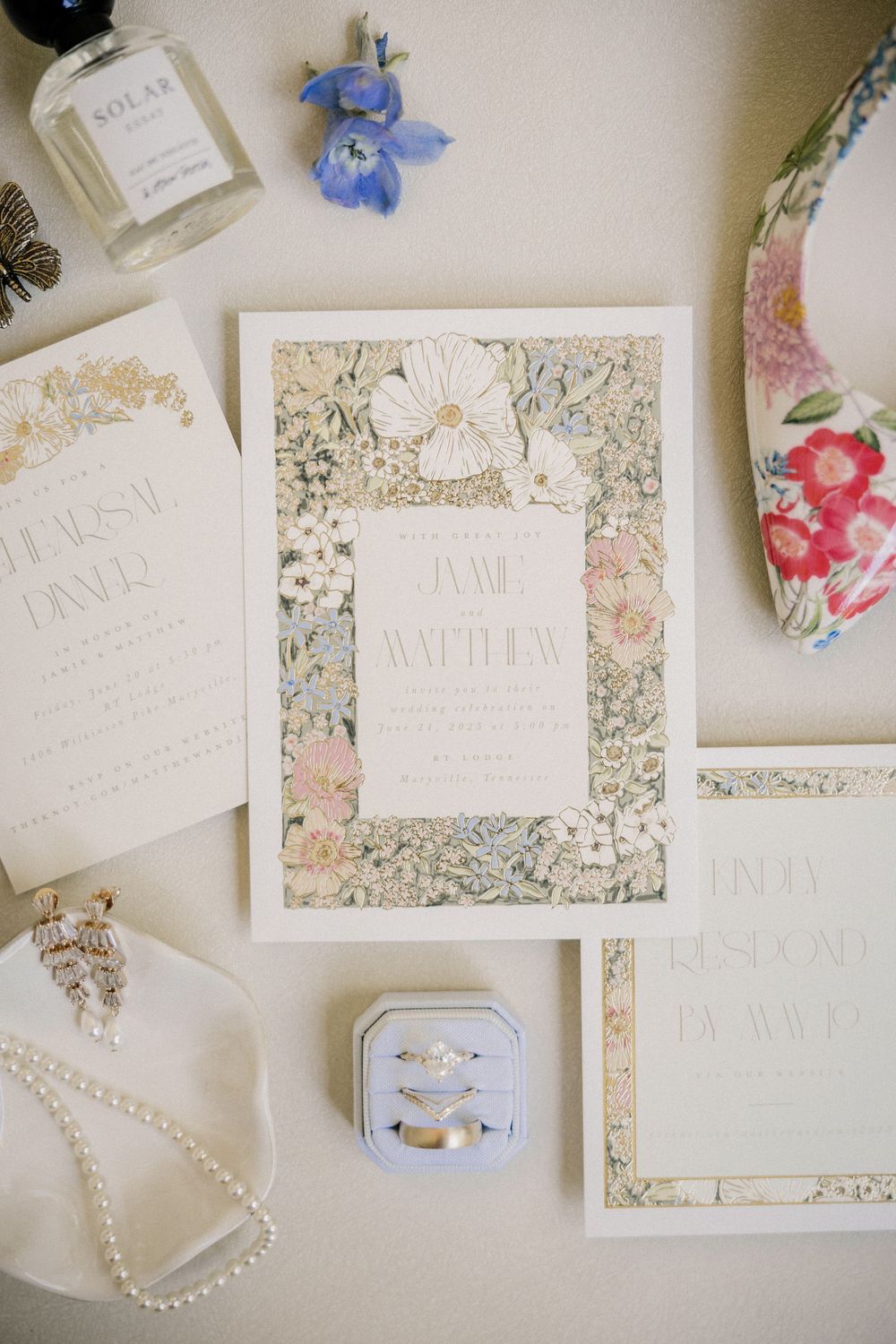 Wedding stationery flatlay with floral designs, invitations, and pearl jewelry on a light beige background.