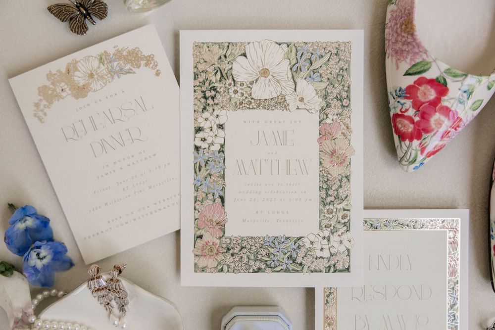 Delicate floral wedding invitations with pink and green botanical designs laid out on a light surface.