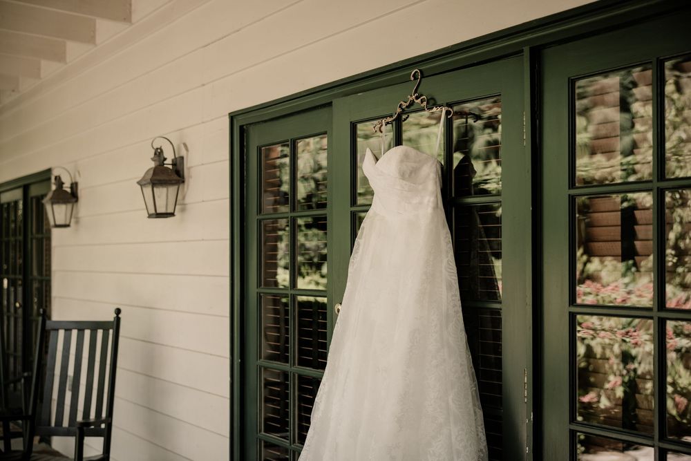 A white wedding dress hangs elegantly on display outside a house with green shutters.