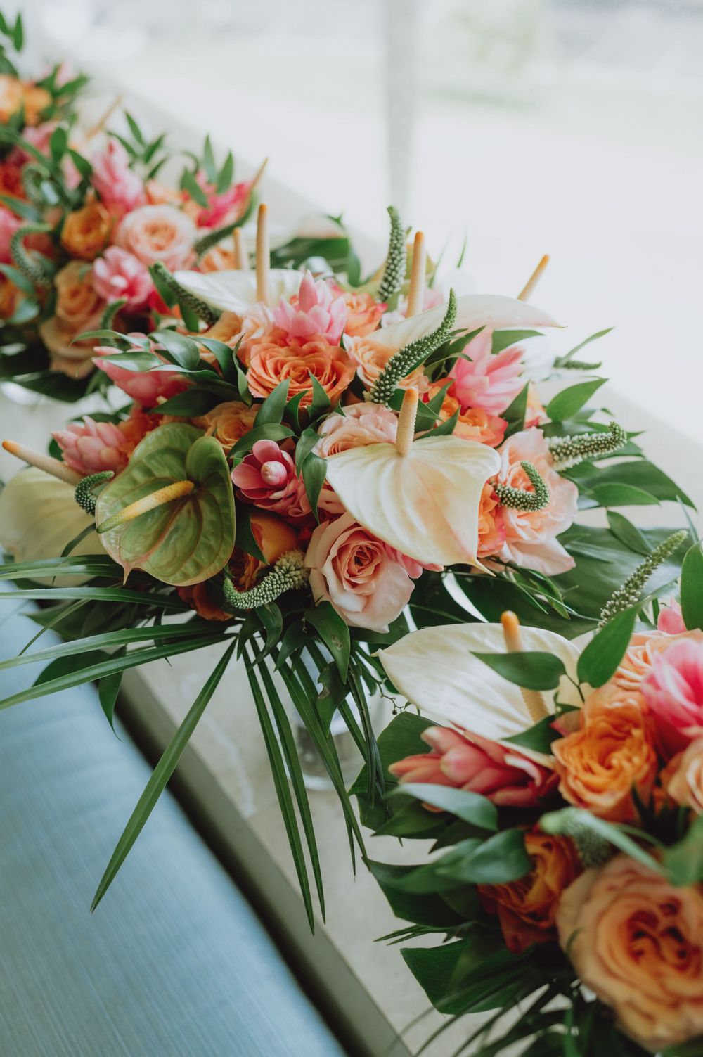 Elegant tropical floral arrangement with coral roses, white lilies and green foliage.