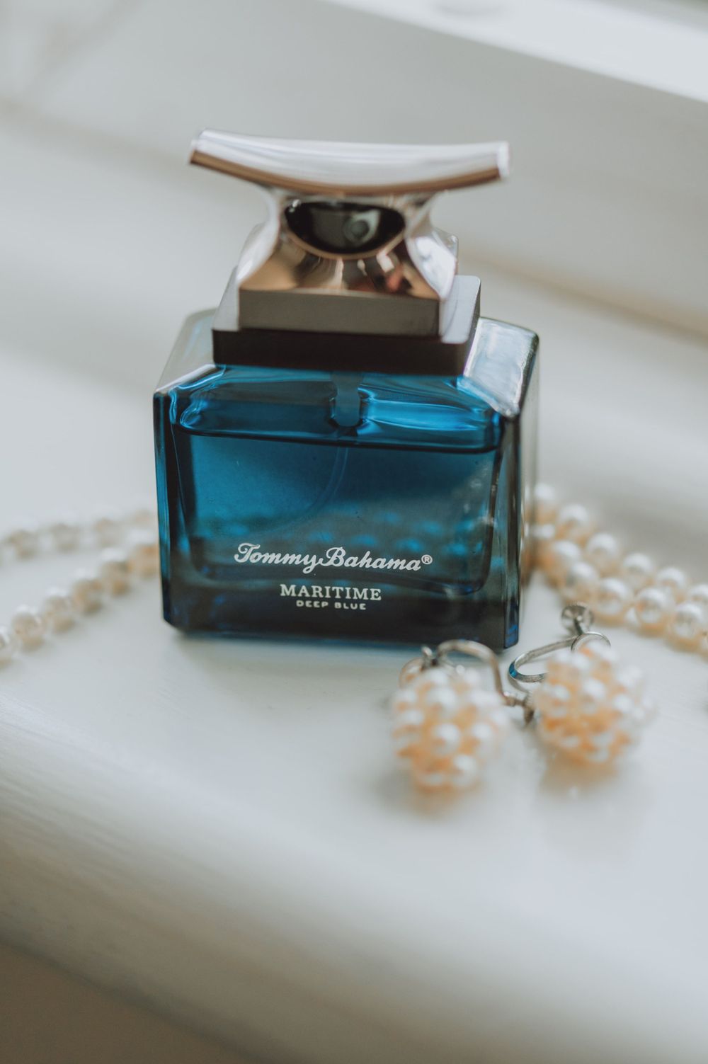 Tommy Bahama cologne bottle with pearl necklace on white surface.