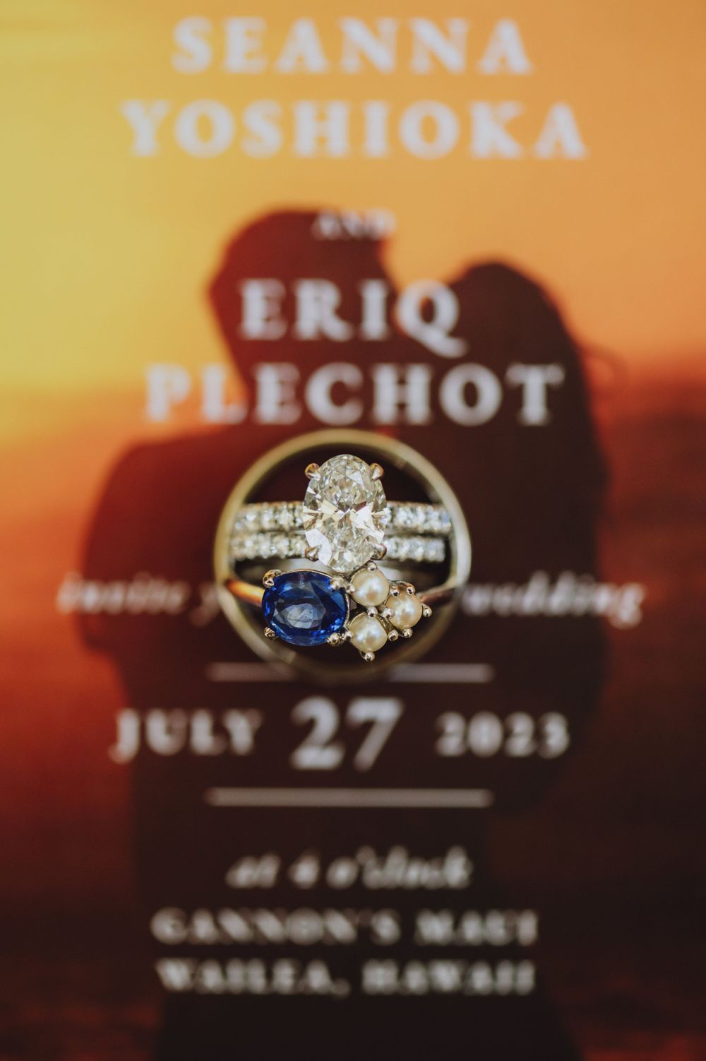 Wedding rings and text details photographed against an orange sunset background.