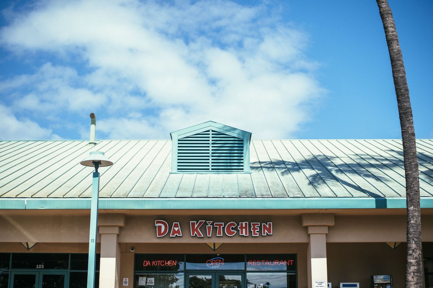 Exterior view of strip mall storefront with white metal roof under blue sky.
