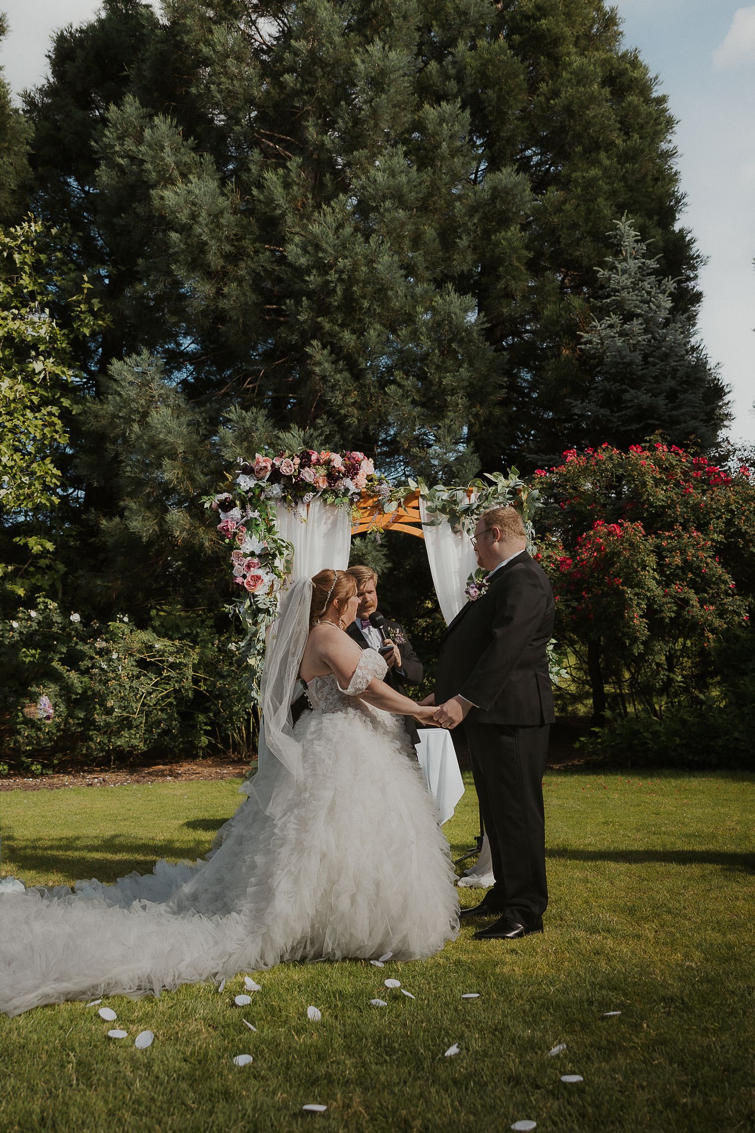 An outdoor wedding ceremony scene with flowing white dress and scattered petals on grass.