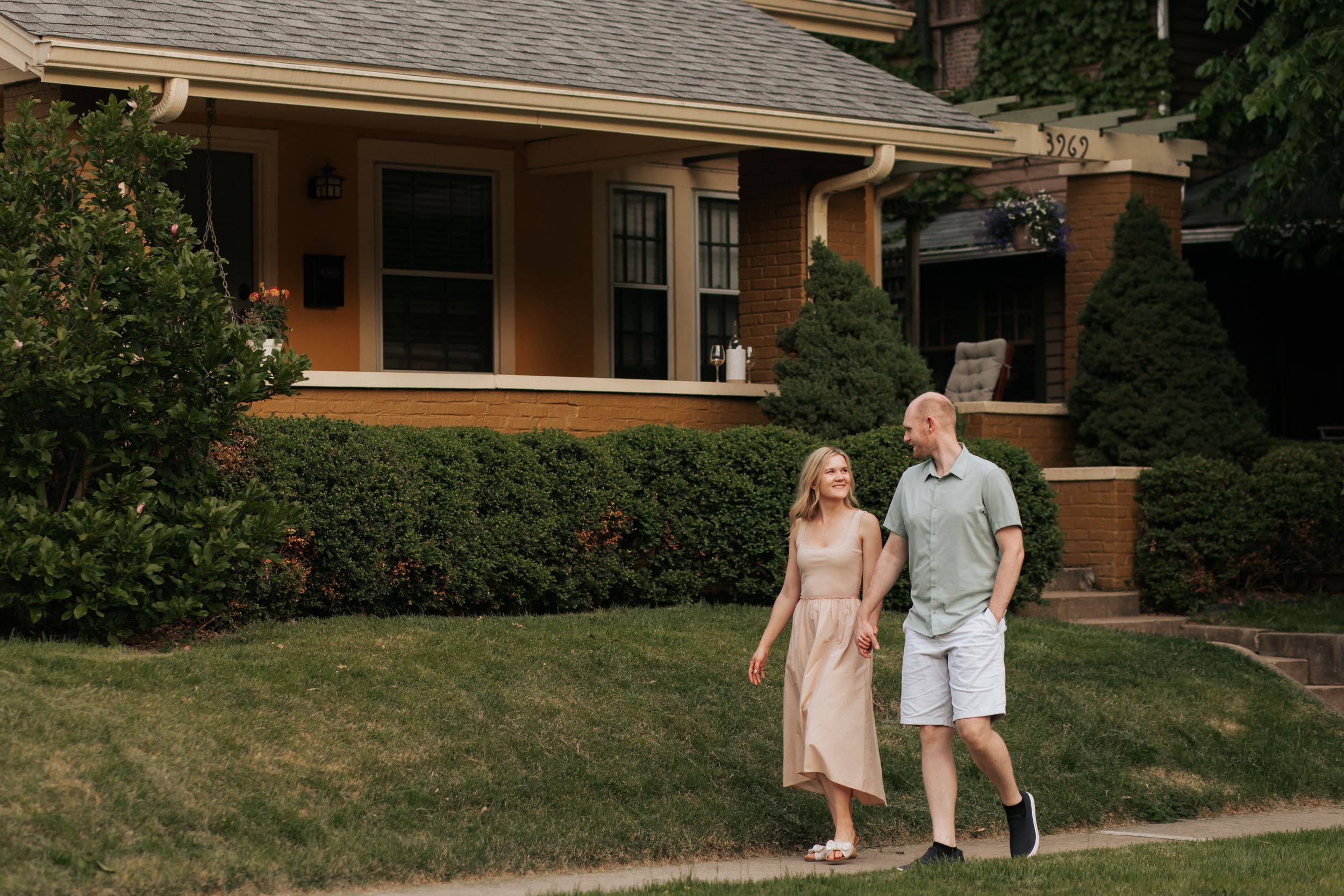 A couple walks along a curved pathway in front of a craftsman style house on a sunny afternoon.