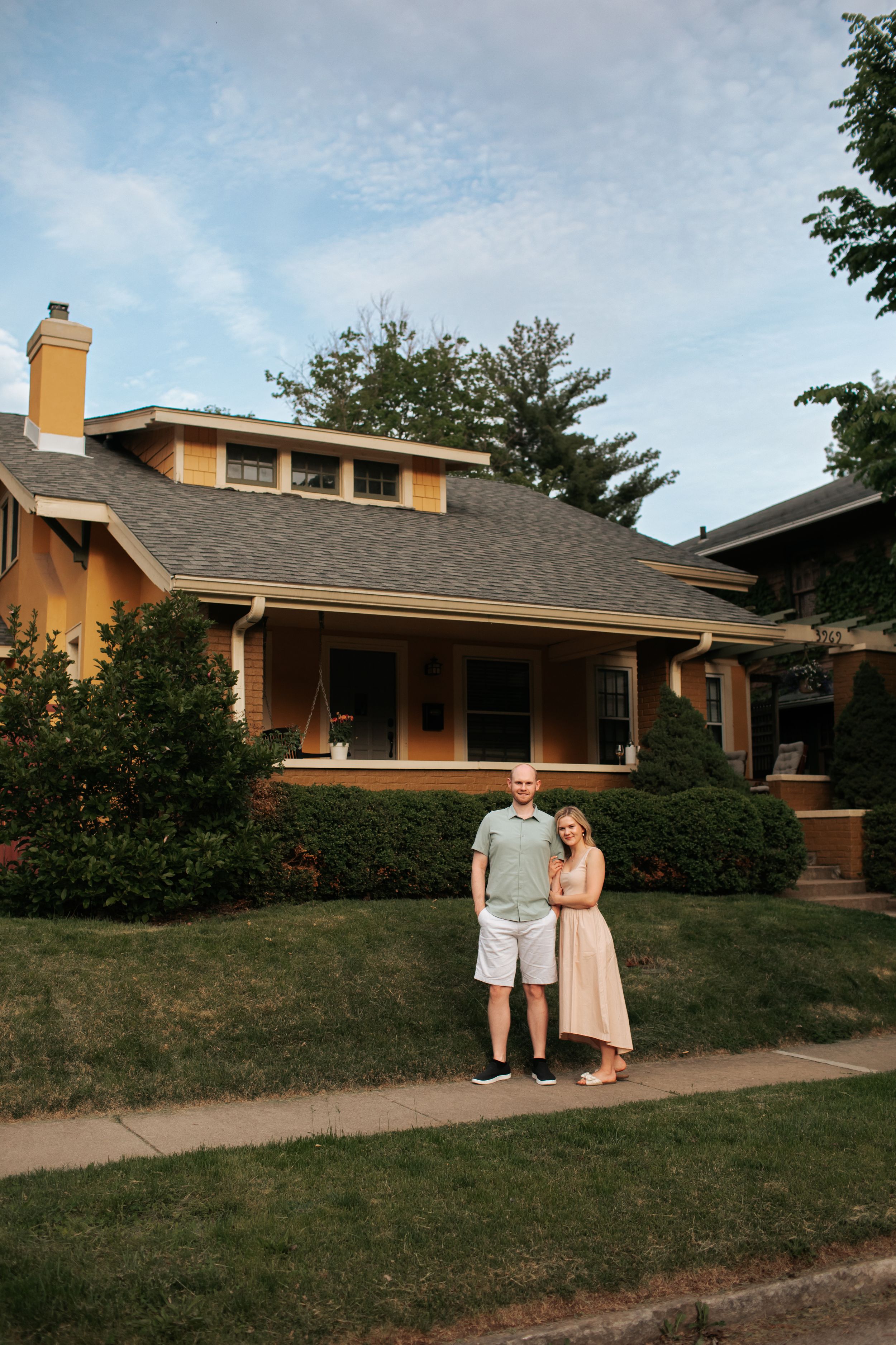 A mid-century ranch style home with orange stucco exterior and dark shingle roof sits on a grassy slope.