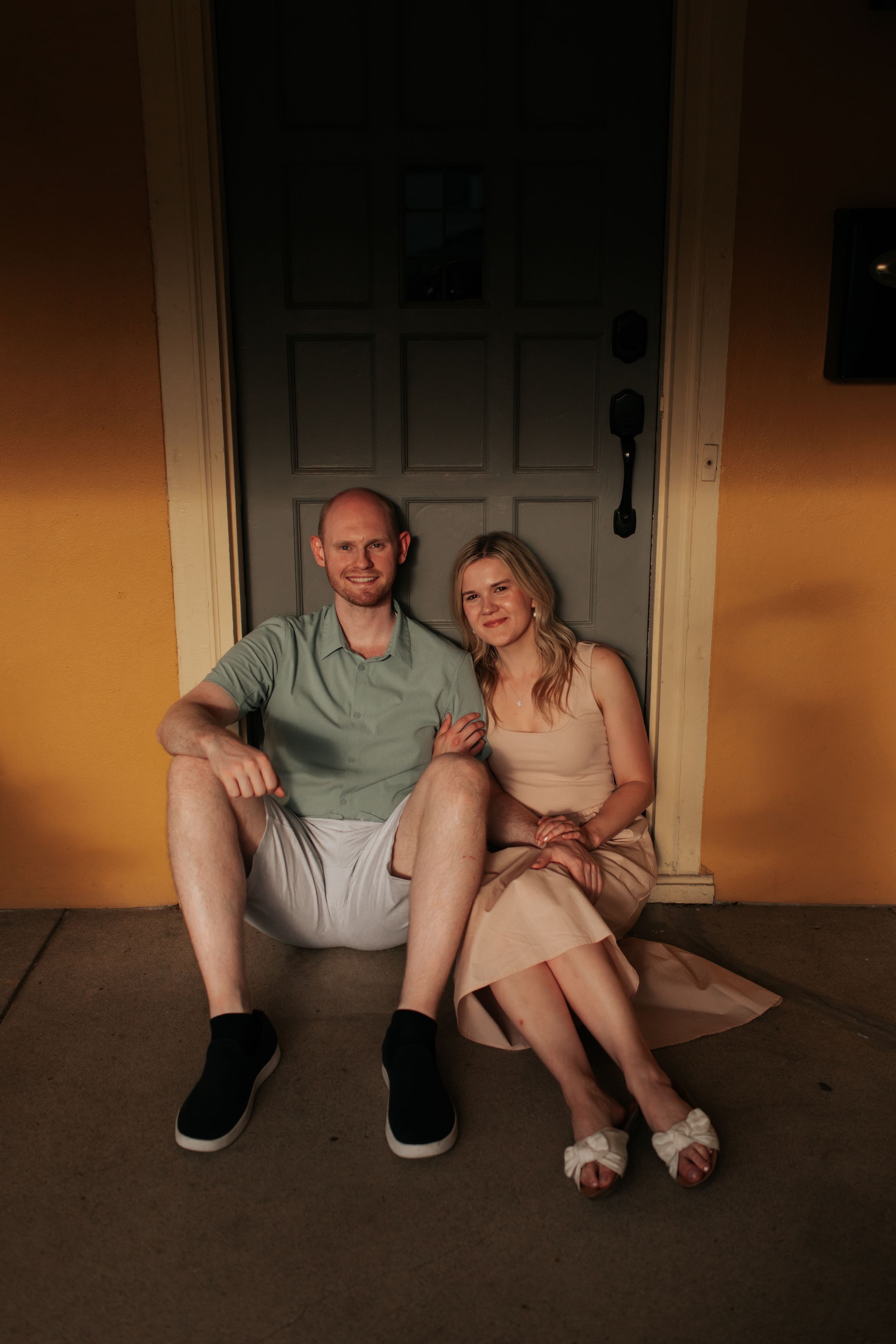 A couple sits together on a porch at sunset, dressed casually in summer attire.