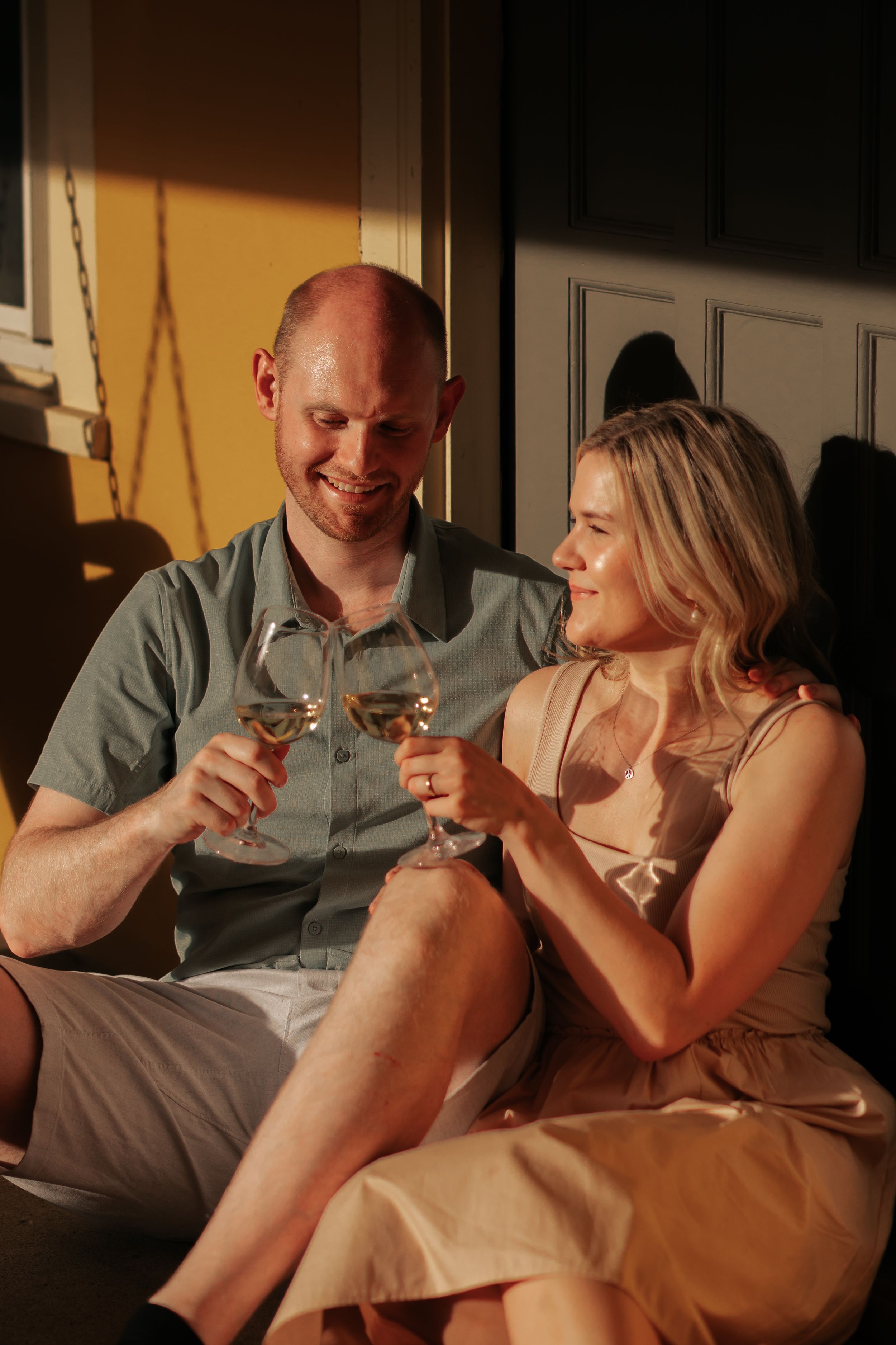 A couple shares a romantic moment while toasting with wine glasses on a dimly lit porch.