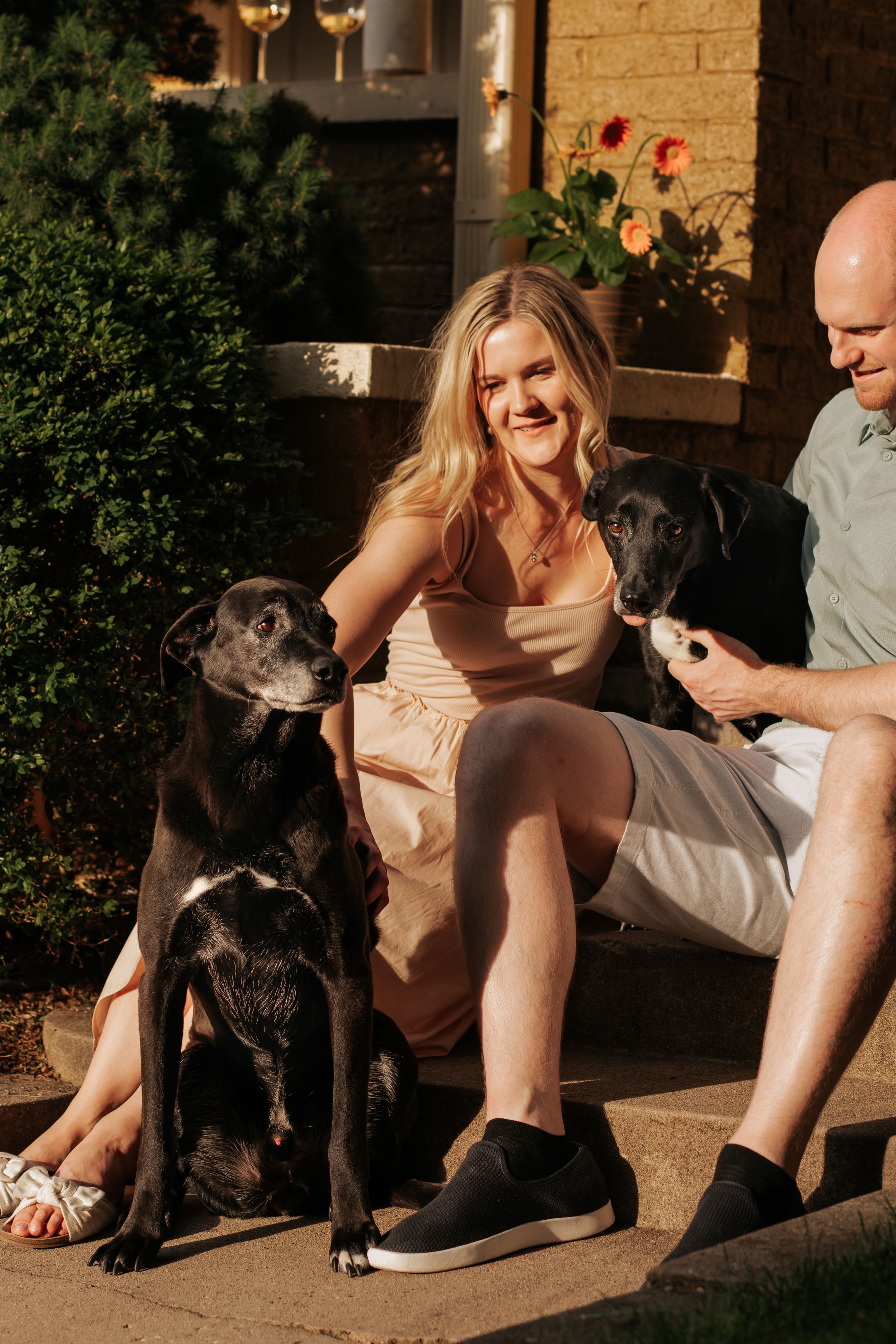 A couple sits on a porch with their black dog during a warm summer evening.