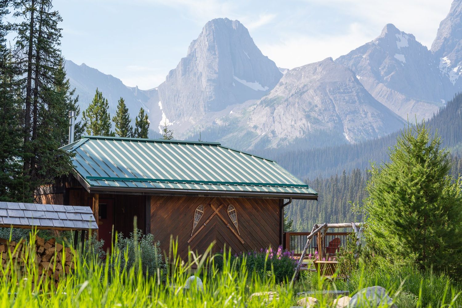 a log cabin in a field with mountains rising behind it in Kananskis, Alberta