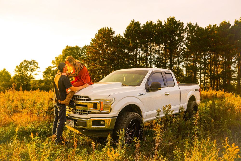 Couple truck photos at golden hour. Couple sitting on top of white truck for poses.