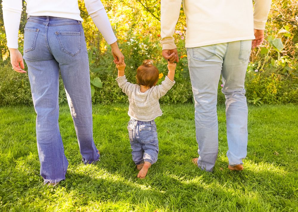 Young family photos with child walking in-between parents holding hands.