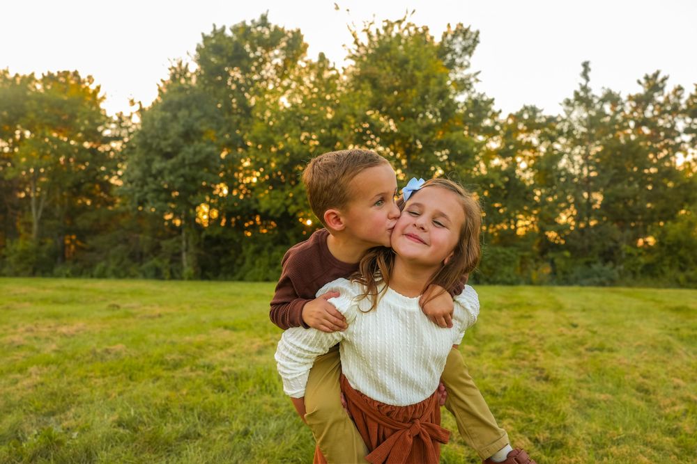 Adorable sibling photo of them giving each other a kiss on the cheek.