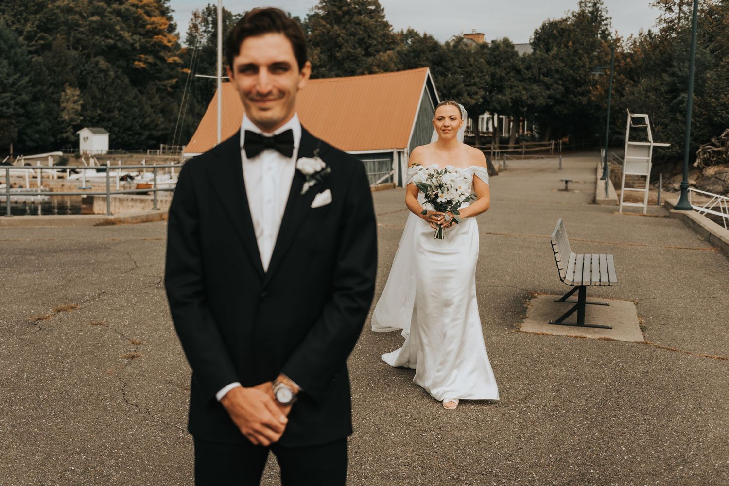 A first look moment between a groom in black tuxedo and bride in white dress at an outdoor wedding venue.