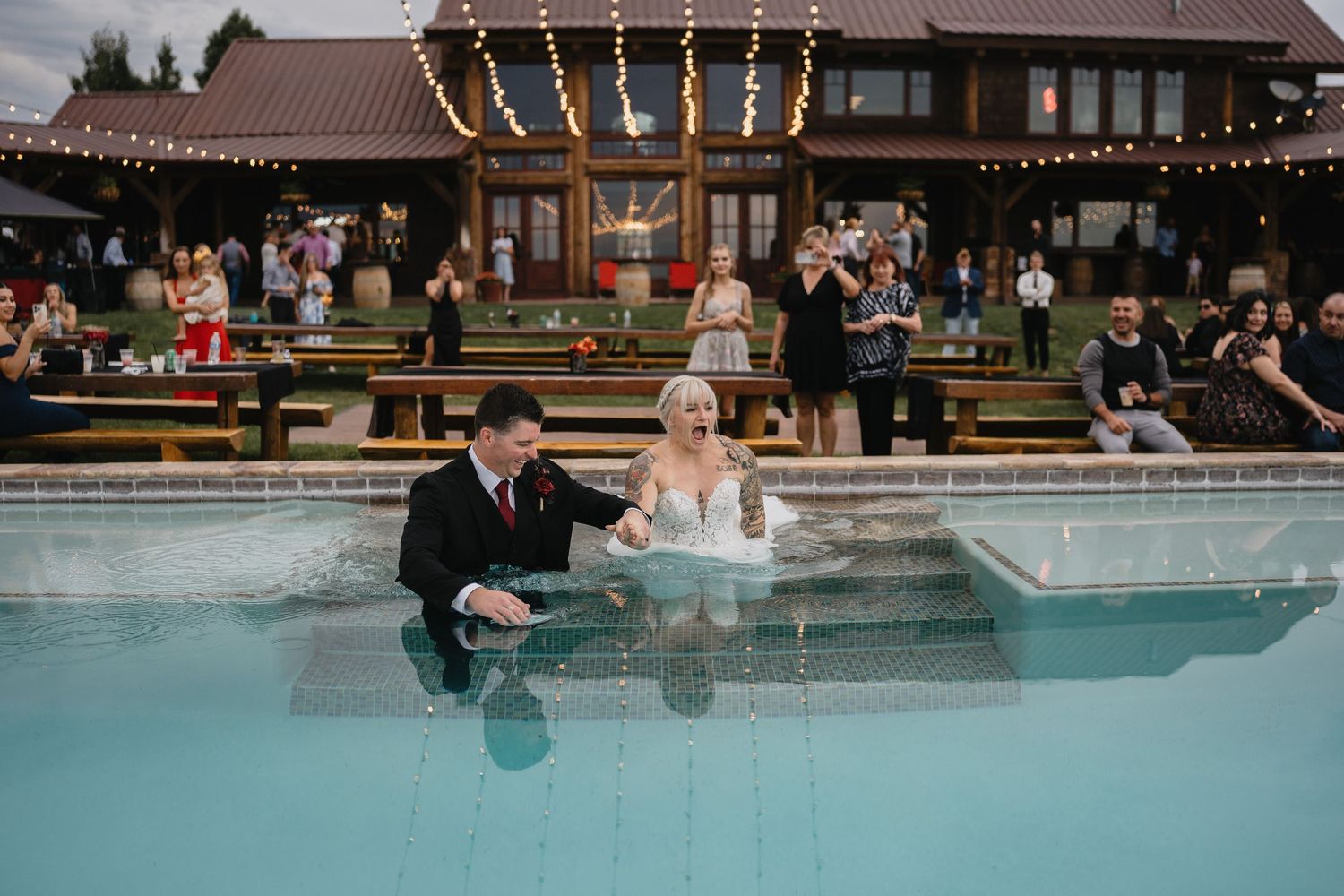 Bride and groom sit together in a sparkling pool at their outdoor wedding reception at dusk at Blame Her Ranch in Santa Fe