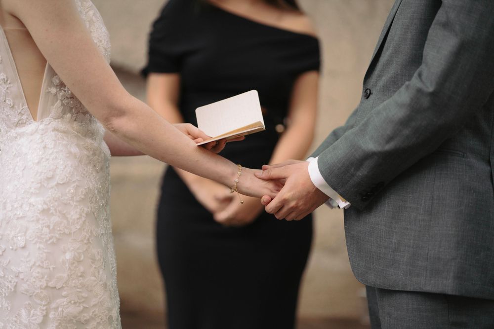 Close-up shot of hands exchanging rings during an intimate wedding ceremony with an officiant in black.