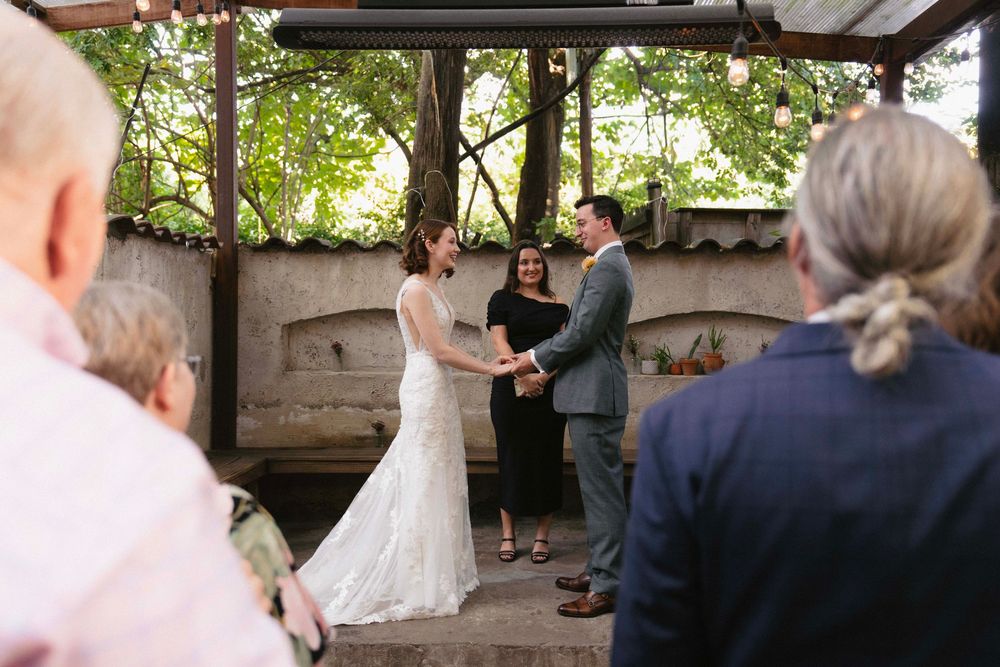 Wedding ceremony taking place under a rustic covered pavilion surrounded by trees.