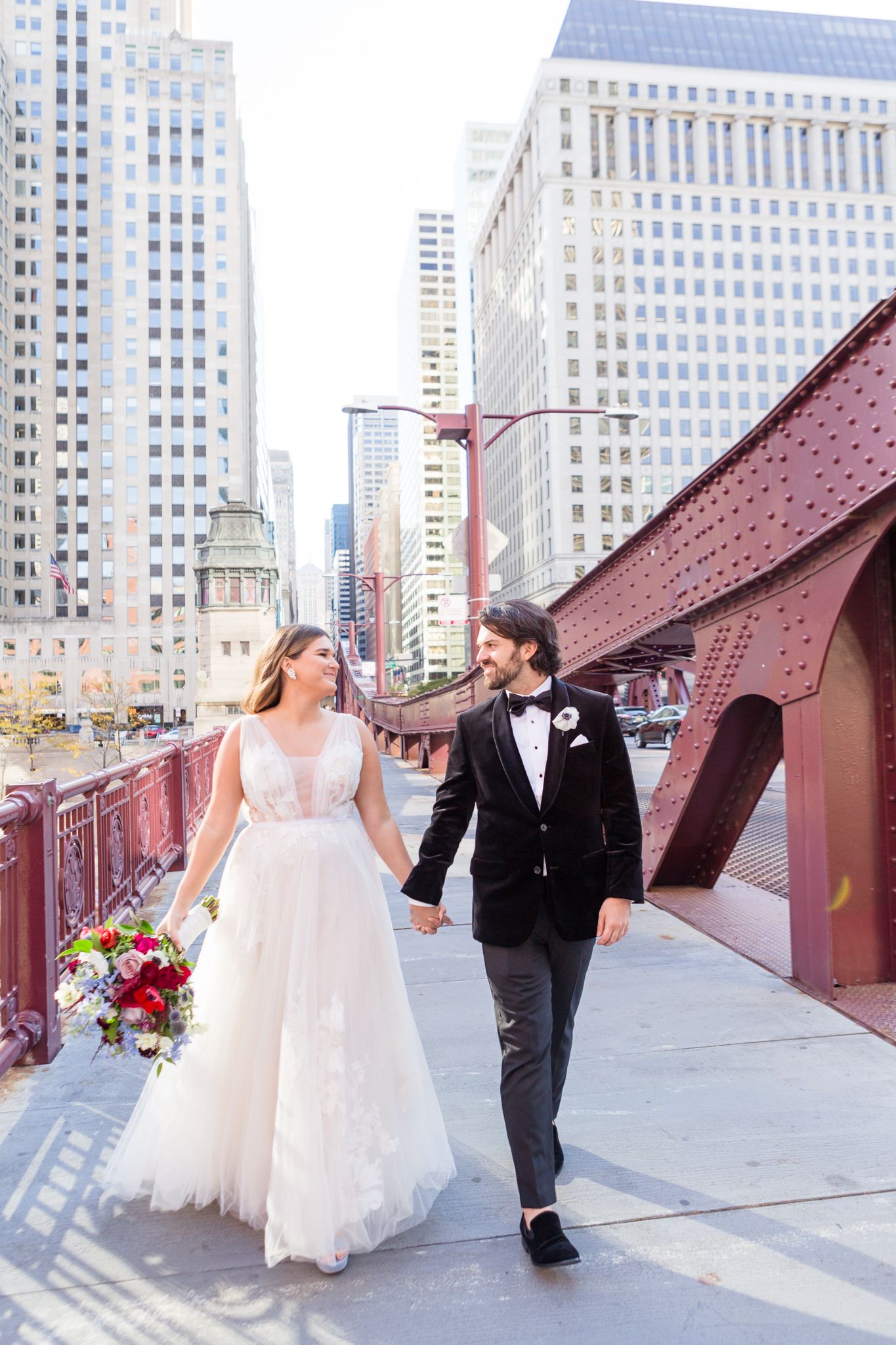 A couple walking along a red-painted walkway with city skyscrapers in the background.