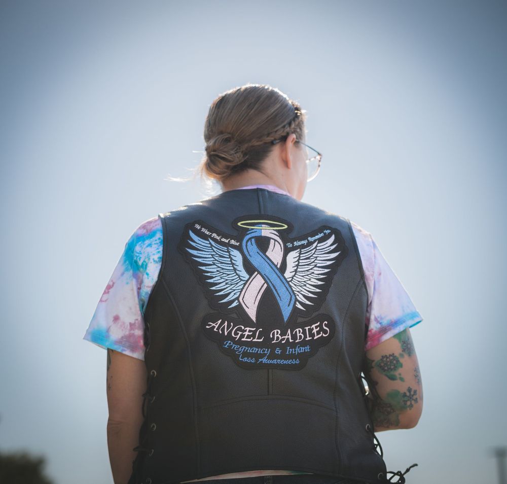 A motorcycle rider wearing a vest with angel wings and ribbon design on the back.