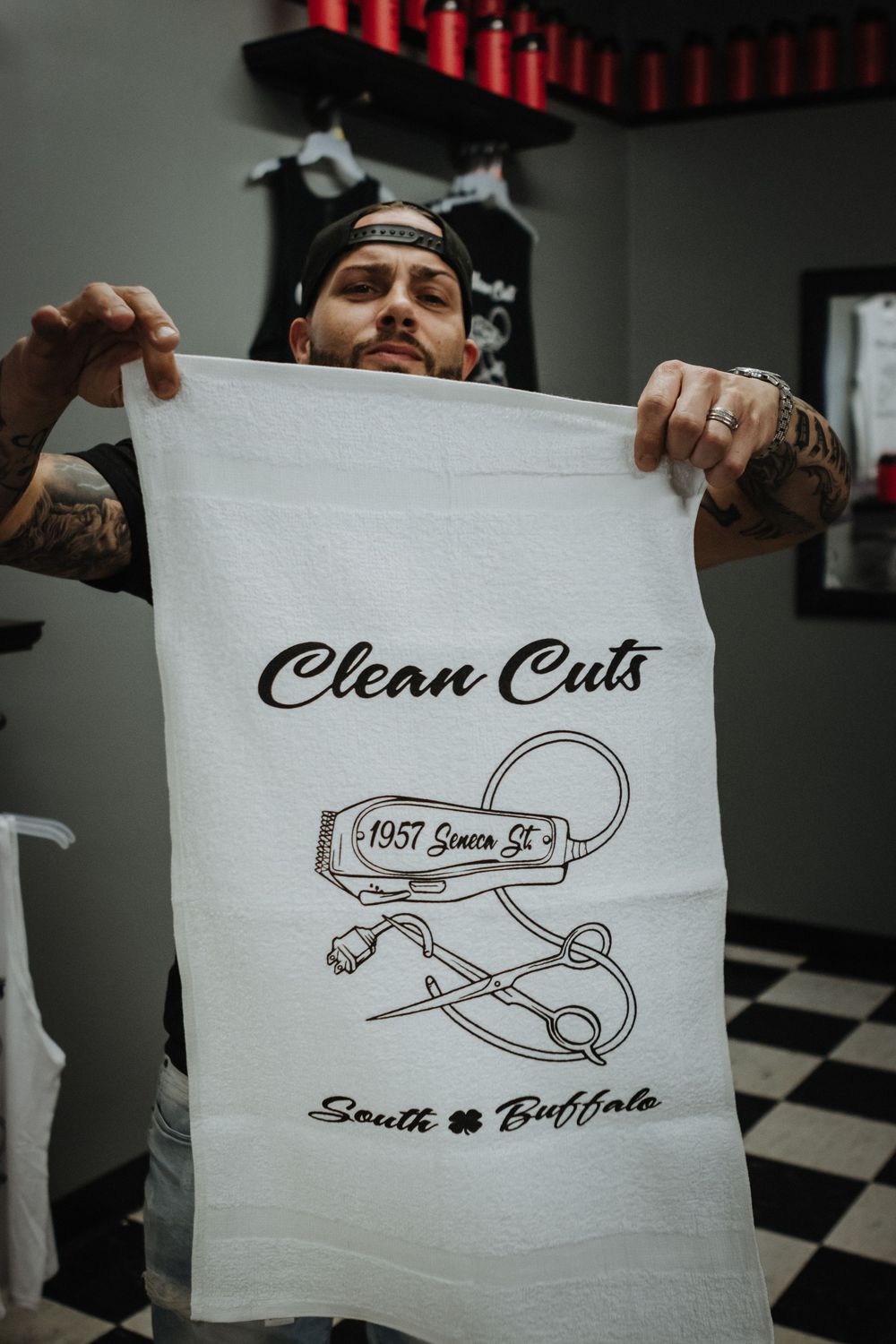 Person holding up white towel with Clean Cuts barbershop logo and vintage clipper design.