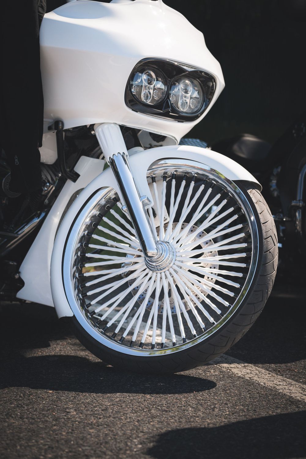 Close-up of a custom white motorcycle wheel with elaborate spoke design and dual headlights.